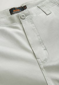 Pantalones cortos de algodón gris claro con cierre de botón, parte delantera plana y detalles de costura visibles. Etiquetados como "Next Durable Goods."
