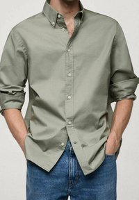 Lichtgroen overhemd met lange mouwen, opgerold bij de manchetten, met een kraag en voor knopen, gecombineerd met een blauwe spijkerbroek.