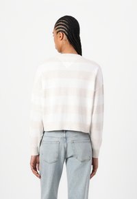 Suéter recortado a rayas en beige claro con rayas blancas. Textura de punto suave, mangas anchas y un detalle en la espalda en forma de V. Combinado con jeans claros.