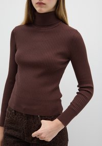 Brauner, gerippter Rollkragenpullover mit langen Ärmeln und figurbetontem Design, aus einem weichen Material. Kombiniert mit dunklen, leopardenprint Hosen.