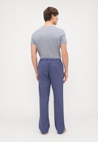 Camiseta de homem cinza de manga curta combinada com calças de pijama de xadrez azul com cintura elástica, em tecido de algodão, de corte relaxado.
