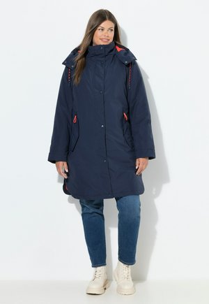 Manteau long marine avec col haut, présentant des accents rouges, des poches latérales zippées et des boutons-pression, fabriqué en tissu lisse et texturé.