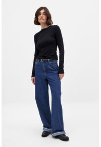 Top negro de manga larga combinado con jeans anchos de color azul. Los jeans tienen una cintura alta, puños de un azul claro y un cinturón visible. Textura de tela lisa.