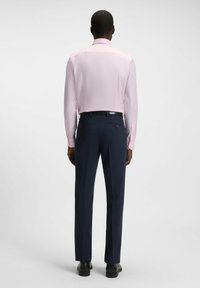Jasnoróżowa koszula z długim rękawem zestawiona z ciemnogranatowymi spodniami. Koszula ma klasyczny kołnierzyk oraz mankiety zapinane na guziki. Dopasowany krój, gładka tekstura.