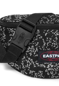 Svart tygmidjeväska med ett prickigt grått mönster, dragkedjestängning, justerbar rem och Eastpak-logotyp. Hållbart material.