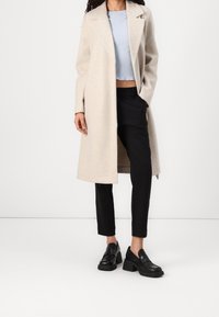 Beige ullblandad kappa med slagkrage, bärs över en ljusblå ribbad crop top och svarta tapered byxor. Svarta loafers med kraftiga klackar.