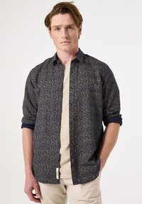 Camisa de botones en color marino con un patrón de hojas y mangas enrolladas. Fabricada con un material liviano y un corte relajado. Etiquetas visibles en la parte inferior.