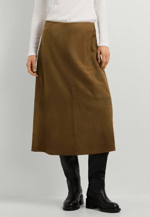 Mujer que lleva una falda midi de ante marrón combinada con botas negras de cuero hasta la rodilla y una camiseta blanca de manga larga.
