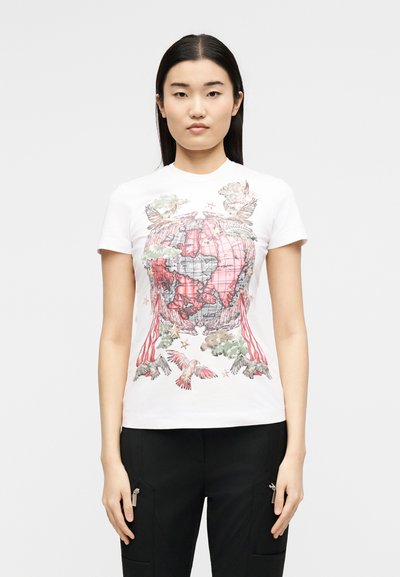 Γυναίκα με ίσια σκούρα μαλλιά φοράει λευκό κοντομάνικο με κόκκινο και γκρι γραφικό παγκόσμιου χάρτη με πουλιά, αστέρια, σύννεφα και ριγέ κορδέλες.