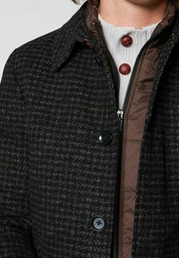 Abrigo de pata de gallo oscuro con acentos marrones. Presenta un cuello estructurado, grandes botones y una capa interior con cremallera. Tejido texturizado.