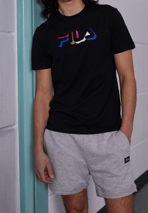 Camiseta negra con logo 'Fila' estilizado y multicolor. Pantalones cortos grises con un parche de logo bordado. Tejido suave, corte relajado.