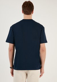 Tricou bleumarin cu mânecă scurtă, confecționat din bumbac moale. Are un guler rotund și o croială lejeră, cu o textură netedă și fără modele vizibile.