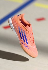 Scarpa atletica arancione con accenti blu, caratterizzata da una tomaia testurizzata, un design a strisce prominente e una silhouette a profilo basso.