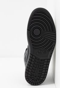 Musta lenkkarikenkä, jonka pohjassa on ympyränmuotoinen logo, kuvioitu pito ja erottuvat kulutuspohjan urat; kumimateriaalia, jossa korostetut harjanteet.