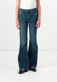 Høytlivede bukser med bredde i bena i mørk blå denim, med fem lommer, kontrastsøm og en ren finish. Flate svarte sko er på.