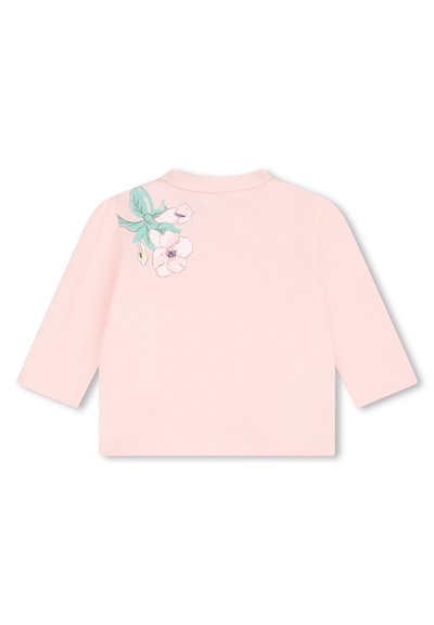 Haut rose clair à manches longues avec un col rond et une broderie florale comportant des feuilles vertes et des fleurs blanches sur l'épaule gauche.