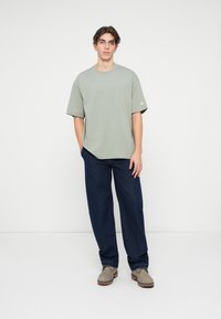 Tricou scurt cu mânecă scurtă, de culoare verde deschis, cu guler rotund și un logo mic; asortat cu blugi negri cu picior larg și încălțăminte gri.