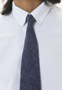 Chemise bleu clair à boutons avec un col évasé, assortie d'une cravate texturée bleu foncé avec un motif tissé subtil.