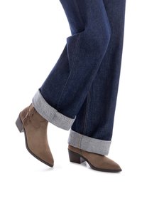 Botines de ante marrón con detalle de flecos, punta afilada y tacón de bloque de 5 cm, combinados con unos jeans de mezclilla azul oscuro con el dobladillo enrollado.