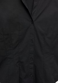 Črna oprijeta srajca z navpičnimi šivi in petimi vidnimi črnimi gumbi po sredini sprednjega dela.