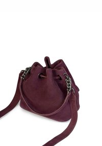Paarse suède emmergeltas met kettingaccenten, trekkoordsluiting en een enkele schouderriem. Zachte textuur en ronde vorm.