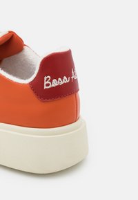 Orange och röd sneaker med en texturerad, mjuk inredning och en vit logotyp. Har en kraftig, benvit sula och en slät syntetisk ovansida.