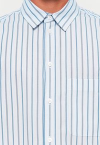 Light blue and white striped shirt featuring a button-up front, spread collar, and a chest pocket. Material appears smooth and lightweight.