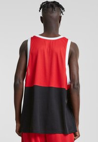 Rød og svart ermeløs basketballtrøye med hvite detaljer. Teksturert mesh-stoff, løs passform og unik fargeblokkdesign.