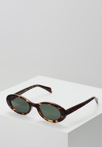 Gafas de sol de carey con forma ovalada redondeada, lentes verde oscuro y patillas delgadas con un acabado brillante y detalles de diseño sutiles.