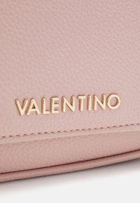 Borsa in pelle texturizzata rosa con logo "Valentino" dorato. Presenta cuciture visibili e un design elegante. La vista ravvicinata mette in evidenza i dettagli del materiale.