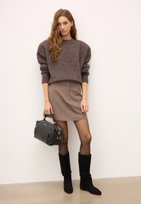 Rudas megztinis su pūstomis rankovėmis, šviesiai ruda sijonas, juodi kelio ilgio batai ir juoda rankinė su auksinėmis detalėmis. Paprastos tekstūros ir spalvos.