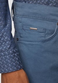 Blå bomullsskjorta med ett texturerat mönster, matchad med mörkblå bomullsbyxor som har en ficka och en metallremsa med "BOSS"-logotyp.