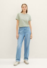 T-shirt vert clair à manches courtes avec le logo "TOM TAILOR", associé à un jean bleu taille haute et des baskets crème.