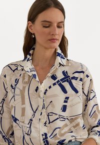 Blouse à manches longues en tissu léger avec un fond crème et un motif de ceinture abstrait bleu marine et beige. Col classique et patte de boutonnage.