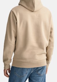 Sudadera con capucha beige de textura suave, con bolsillo tipo canguro, puños y dobladillo acanalados, diseñada con un ajuste relajado para mayor comodidad.