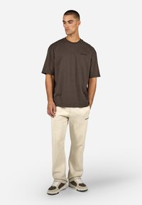 Barna, rövid ujjú póló, kis logóval a mellrészen, tejszínszínű melegítőnadrággal és vastag bézs sportcipővel párosítva.