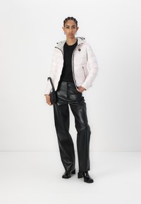 Giacca puffer rosa chiaro con cappuccio grigio, maglietta nera a maniche lunghe e pantaloni in ecopelle neri a vita alta. Stivaletti neri alla caviglia e borsa piccola.