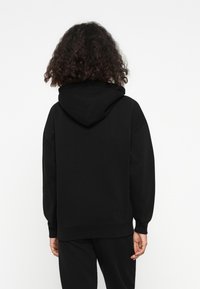Felpa nera con cappuccio, dal taglio rilassato, con tasca a marsupio e polsini a costine. Materiale morbido e design minimalista.