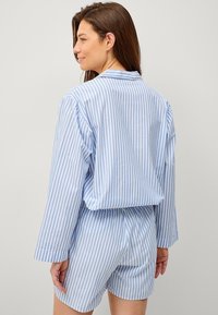 Blå og hvid stribet pyjamas sæt med en langærmet skjorte med knapper og matchende shorts med elastisk talje.