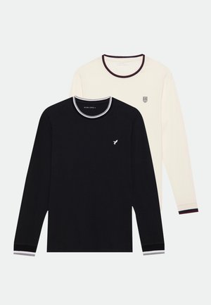 Two long-sleeve tops: one black with a crew neck and white accents, and one cream with a logo and contrasting ribbed hem.