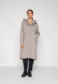 Világosszürke, hosszú kabát kapucnival, elülső cipzárral és húzózsinóros szegéllyel. Oldalzsebekkel és laza szabással rendelkezik. Fekete nadrág és cipő fölött viselve.