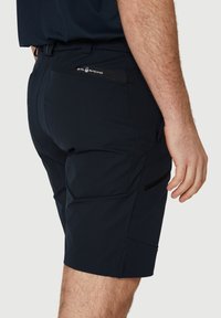 Shorts tummansinisestä, kevyestä ja teksturoidusta kankaasta. Ominaisuuksiin kuuluu useita taskuja, tyylikäs muotoilu ja hillitty brändilogo takana.