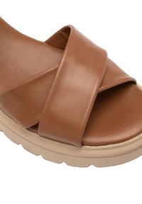 Pruun nahkne libisev sandaal ristkasutatud rihmadega, pehme jalatoega ja paks beige kummitald. Pind on sile ja kerge läikega.