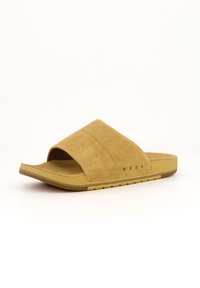 Sandale à glissière en suède tan avec un bout ouvert, semelle plate et logo 'REEF' sur le côté. Design simple et moderne avec une finition texturée.