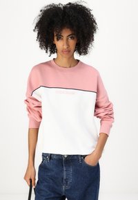 Genser med rund hals, rosa øverste del og hvit nedre del, med en svart horisontal stripe og logo på forsiden.