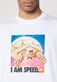 Biała koszulka z kolorową grafiką żółwia w lustrzanych okularach przeciwsłonecznych na tle galaktyki oraz wyraźnym napisem: „I AM SPEED.”
