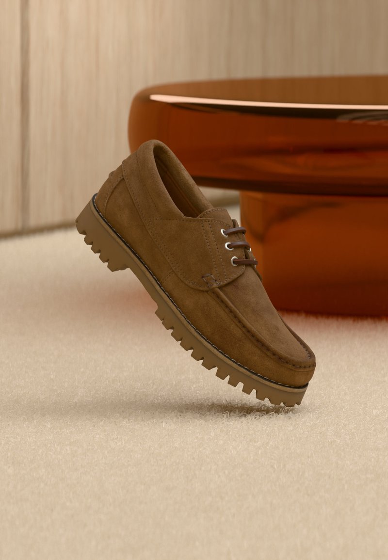 Chaussure à lacets en daim marron avec semelle épaisse et striée flottant au-dessus d'un tapis beige, avec une table ovale marron en arrière-plan.