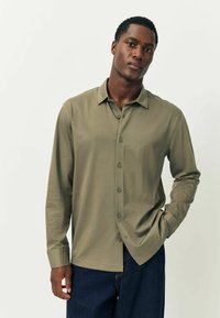 Oliven grøn langærmet skjorte med knap-ned krave, frontknapper og en glat tekstur, parret med mørke denim jeans.