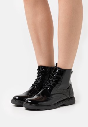 Stivali alla caviglia in pelle verniciata nera con punta arrotondata, design con lacci, dettagli brogue e suola in gomma nera a contrasto.