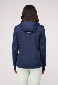 Jūrų tamsiai mėlynas softshell švarkas su gobtuvu, užtrauktukais šoninėse kišenėse ir prigludusia forma. Pagamintas iš lygaus, tamprumo medžiagos, užtikrinančios komfortą.